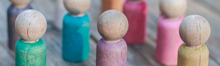Bunte Holzspielfiguren in einer Gruppe auf einem rustikalen Holzuntergrund.