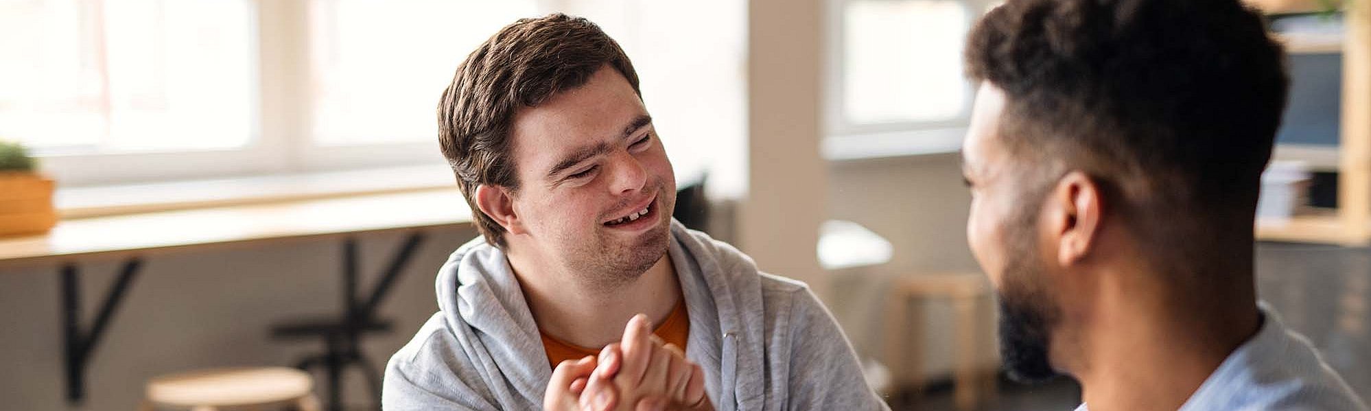 Ein junger Mann mit Down-Syndrom schlägt mit einem anderen Mann und lächelt ihn an.